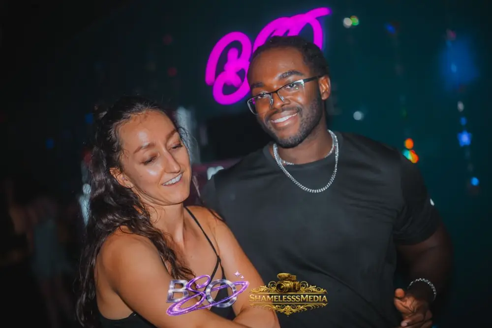 A couple smiling under the pink BSO neon